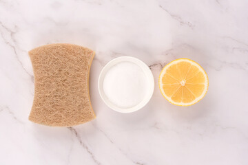 Natural household cleaning bundle with eco ingredients - walnut dishcloth, lemon, baking soda or citric acid over marble countertop table background. Green cleaning concept, selective focus. Flat lay 