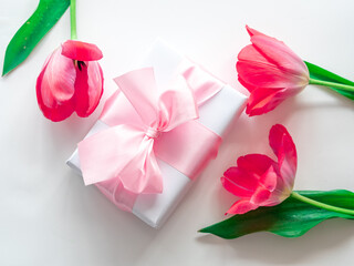 Wrapped gift box with a delicate pink bow and tulips, the concept of a holiday on March 8 or Valentine's Day
