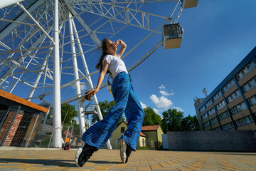 Outdoor photo of young caucasian teenager stand on toes with Ferris wheel in the background in...