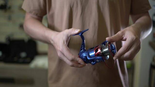 Fishing tackle shop, close-up of a man's hands holding a reel for a fishing rod.