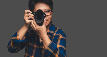 A Photographer holding a digital camera while standing on a gray background