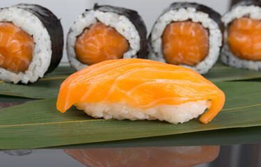 close-up, on a dark table with a reflection, on a green bamboo leaf, sushi and Japanese rolls with salmon