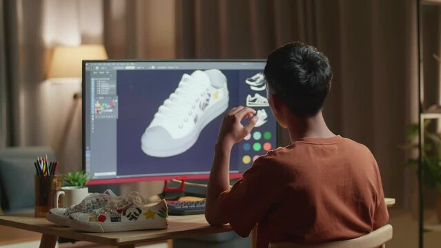 Asian Boy Footwear Designer Rotate 3D Model Of Shoe While Working On A Desktop At Home. Shoe Production Procedure Concept. Cyber Games Clothing And Footwear Line
