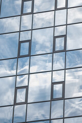 Glazed wall of a building with reflection of clouds in mirrored windows