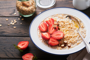 Oatmeal. Bowl of oatmeal porridge with strawberry, almond and milk on old wooden dark table background. Top view in flat lay style. Natural ingredients. Hot and healthy breakfast and diet food.