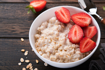 Oatmeal. Bowl of oatmeal porridge with strawberry, almond and milk on old wooden dark table background. Top view in flat lay style. Natural ingredients. Hot and healthy breakfast and diet food.