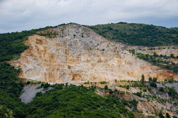 Fototapeta premium Natural quarry is located near road against backdrop of Rhodope Mountains and hills with forests and mountain vegetation