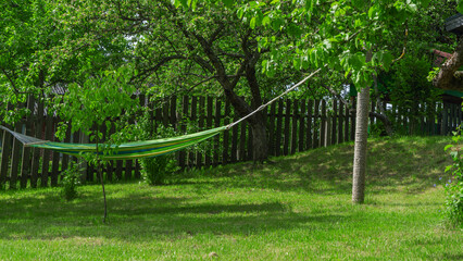 Summer garden with hanging hammock for relaxation. Hammock in backyard on the fence background.