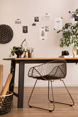The stylish composition of cozy office interior with metal chair, wooden table, plants, pictures and personal accessories. Home decor. Template.