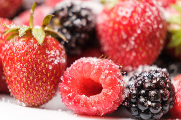 Raspberries, strawberries and blackberries sprinkled with sugar, close-up.