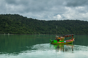 Small fishing boat in the ocean with forest island background.