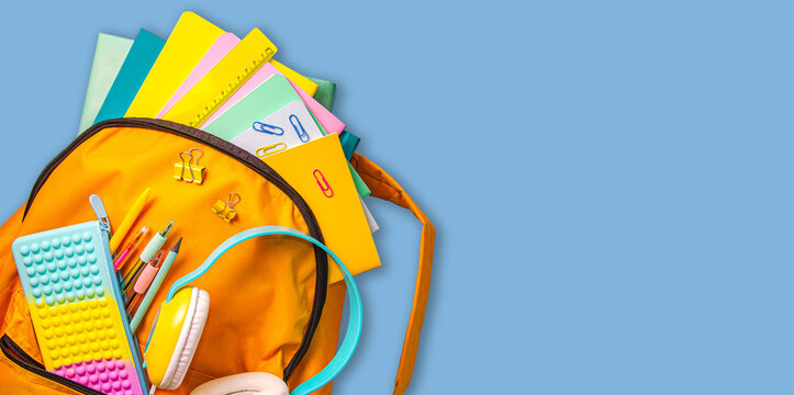 The concept of back to school. Yellow school backpack with notebooks, books, headphones and stationery on a blue background