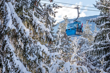 Winter resort with ski lift gondola cabins and snow mountains and pine trees after snowfall,...
