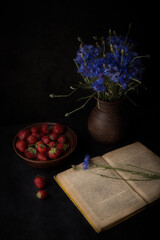 Still life with strawberries and cornflowers on a black background