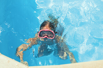 Naklejka premium Child swims in pool underwater, happy active girl in snorkel goggles has fun in water