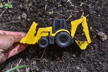 Toy digger with child's hand digging in muddy soil