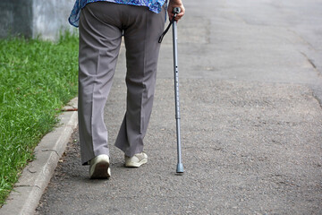 Old woman walking with cane on summer street, legs on sidewalk. Concept of disability, limping adult, diseases of the spine - obrazy, fototapety, plakaty