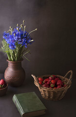 Still life with strawberries and cornflowers on a black background