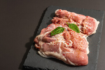 Raw turkey thigh with spices. Fresh boneless meat on a ceramic stand. Hard light, dark shadow