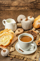 Breakfast concept with a cup of coffee, croissants, milk jug, and decorative crochet pumpkins
