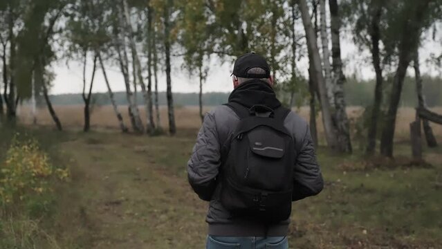 Male tourist walks through the birch grove. Autumn traveler hike with backpack. The unity of human with nature