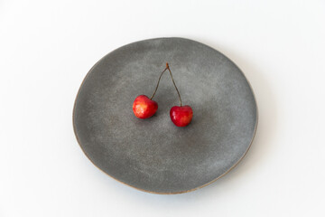 Two ripe fresh cherries with a ponytail in a gray plate on a white background. Healthy food. Vegan breakfast. Close-up.