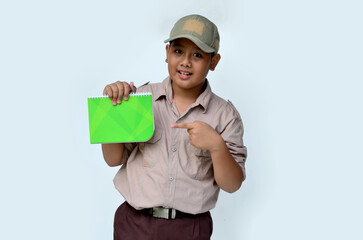 Asian boy in scouting uniform pointing at a green book, isolated white background