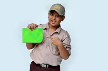 Asian boy in scouting uniform pointing at a green book, isolated white background