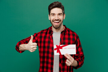 Young happy fun man he 20s in red shirt grey t-shirt hold gift certificate coupon voucher card for store show thumb up isolated on plain dark green background studio portrait People lifestyle concept - obrazy, fototapety, plakaty
