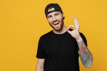 Young satisfied happy positive bearded tattooed man 20s he wears casual black t-shirt cap showing...