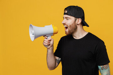 Young bearded tattooed man 20s he wearing casual black t-shirt cap holding scream in megaphone...