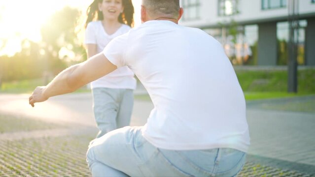 Daughter Runs To Dad And Hugs Him. Father Picks Up The Child In His Arms. Slow Motion