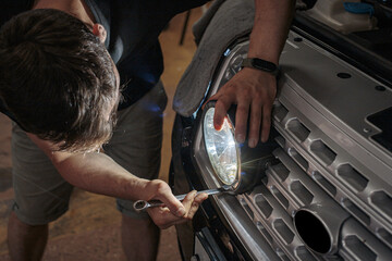 The mechanic is in the process of installing and adjusting the headlights on the car. The process of installing LED optics on a car, selective focus. Repair and restoration of the headlight. © Dmitry Presnyakov