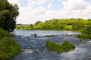 Fototapeta premium Winding river on a riffle in a summer forest in cloudy weather with rain clouds. Landscape in the river forest