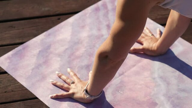 A sporty woman with a smart watch puts her hands on the mat, prepares to do yoga