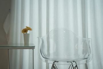 A modern design chair which is made from transparent plastic material, placed on white curtain...