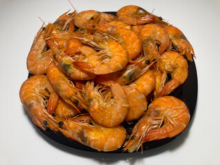 On the white table is a black plate full of big, juicy, boiled shrimp. A great appetizer for a beer party.