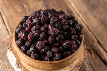 The black berry is a hybrid of raspberries and blackberries. Berries in a wooden bowl on the table. Vitamin summer food. Harvest. Raspberry and blackberry. Black raspberry.