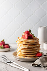 Pancakes stack with fresh strawberries and cutlery at white table, breakfast composition