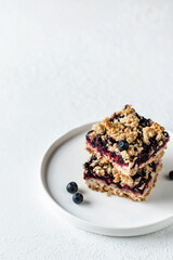Homemade blueberry crumble bars on a plate on white textured background isolated with text space