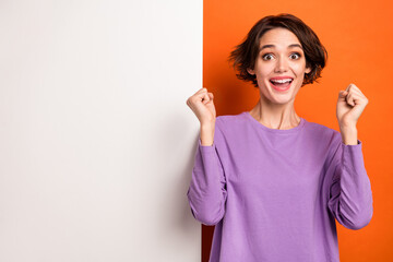 Photo of gorgeous lucky lady wear violet sweatshirt rising fists white poster empty space isolated orange color background