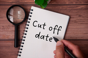 Hand writing cut of date on notepad with table plant and magnifying glass on wooden table. - obrazy, fototapety, plakaty