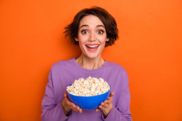 Photo of funny excited girl dressed purple pullover holding popcorn plate isolated orange color background