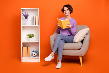 Full length photo of sweet cute lady wear violet sweatshirt sitting chair reading book isolated orange color background