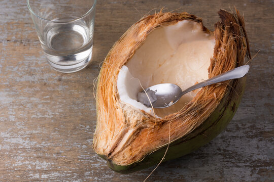 eating young coconut meat straight from the shell with a spoon, white flesh of healthy tropical fruit on a wooden table top, space for text