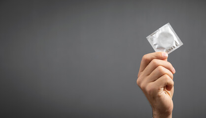 Male hand showing condom on grey background.