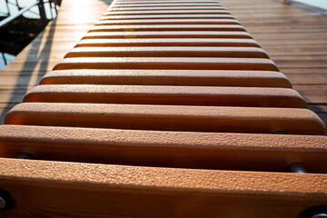 Drops of ross on the boards shine in the rays of the morning sun, a pattern of wood, a wet park bench, a wooden product.