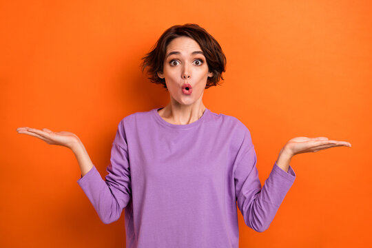 Photo of impressed funky lady wear violet sweatshirt showing arms scales empty space isolated orange color background