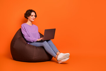 Full size portrait of pretty positive lady sitting cozy bag use wireless netbook isolated on orange...