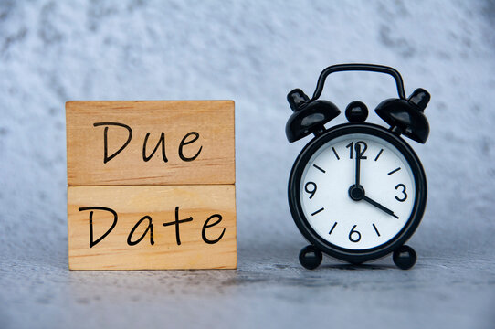 Alarm clock pointing at 4 o'clock with text on wooden block - Due Date.